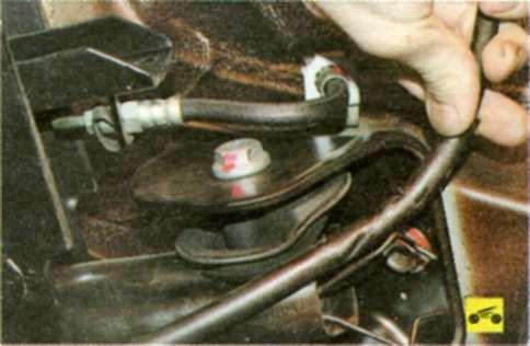 Извлеките задние тросы привода стояночного тормоза из держателей на кронштейнах крепления балки задней подвески к кузову