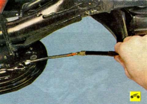 Извлеките один наконечник троса из отверстия защитного щитка заднего тормозного механизма
